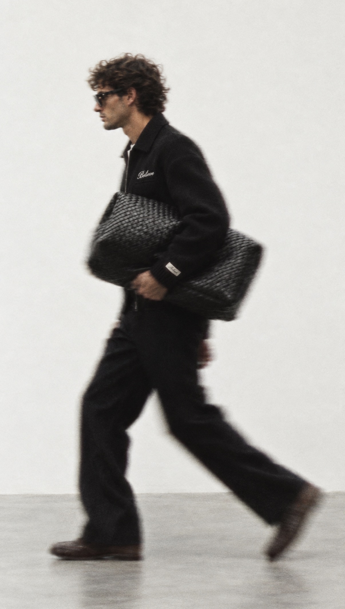 BELIEVE model walking in the black wool jacket, carrying a woven bag